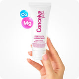 For Conceive Plus Fertility Lubricant Tube + Applicators bundle, the image shows the 75ml multi-use tube being held upright by a hand. The product is displayed clearly with pink branding on a white tube, accompanied by icons showing calcium and magnesium ions on a soft white background.